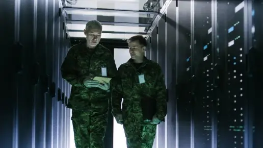 Two military officers walking down a long row of server racks.